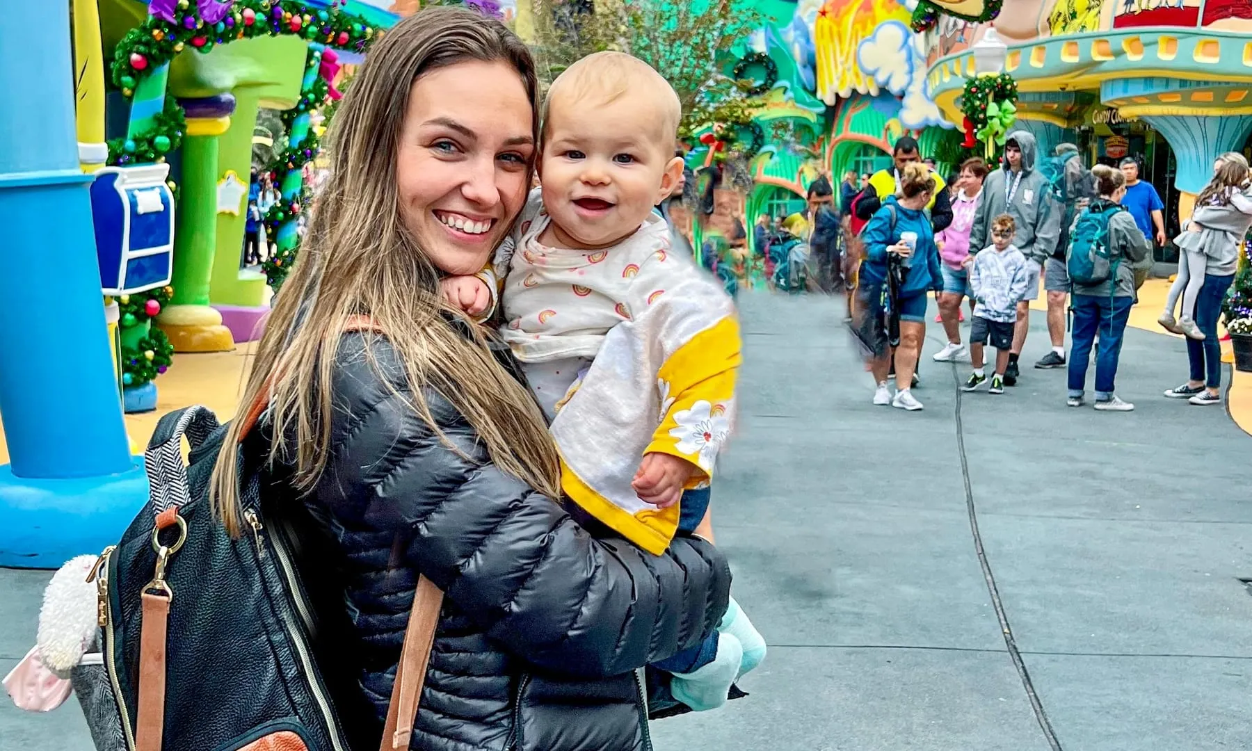 Kiersten carrying baby Addie in a hip carrier down a brightly coloured theme park street